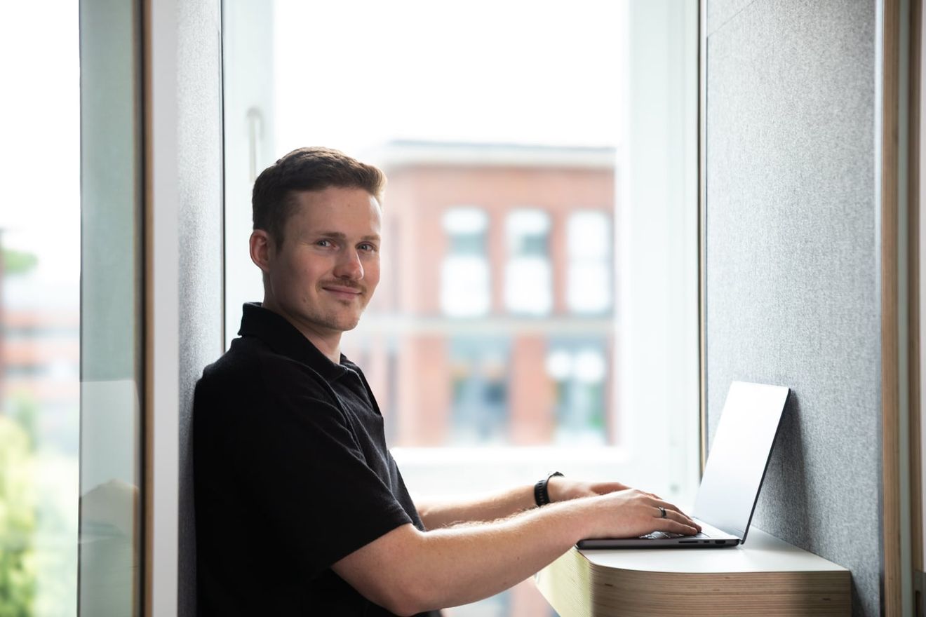 Tim Schauder arbeitet am Laptop an einem Fensterplatz im Büro